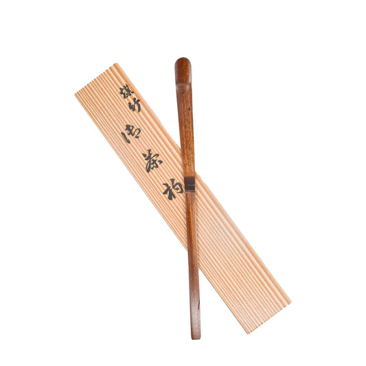 A black bamboo chashaku matcha scoop laid next to its protective sheath, both featuring Japanese characters.